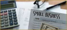 Small business tax documents with calculator, financial records, and cash on a desk.