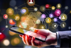 A smart phone held in a hand with several icons of social media and networking in the background.