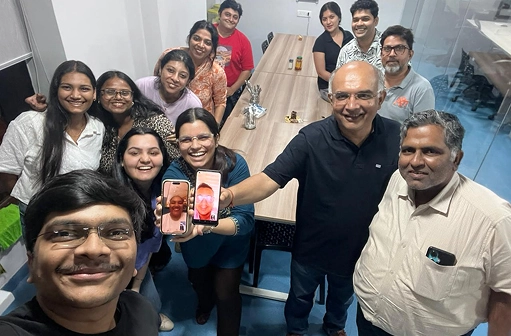 A group of people smiling for a selfie with a camera phone in hand.